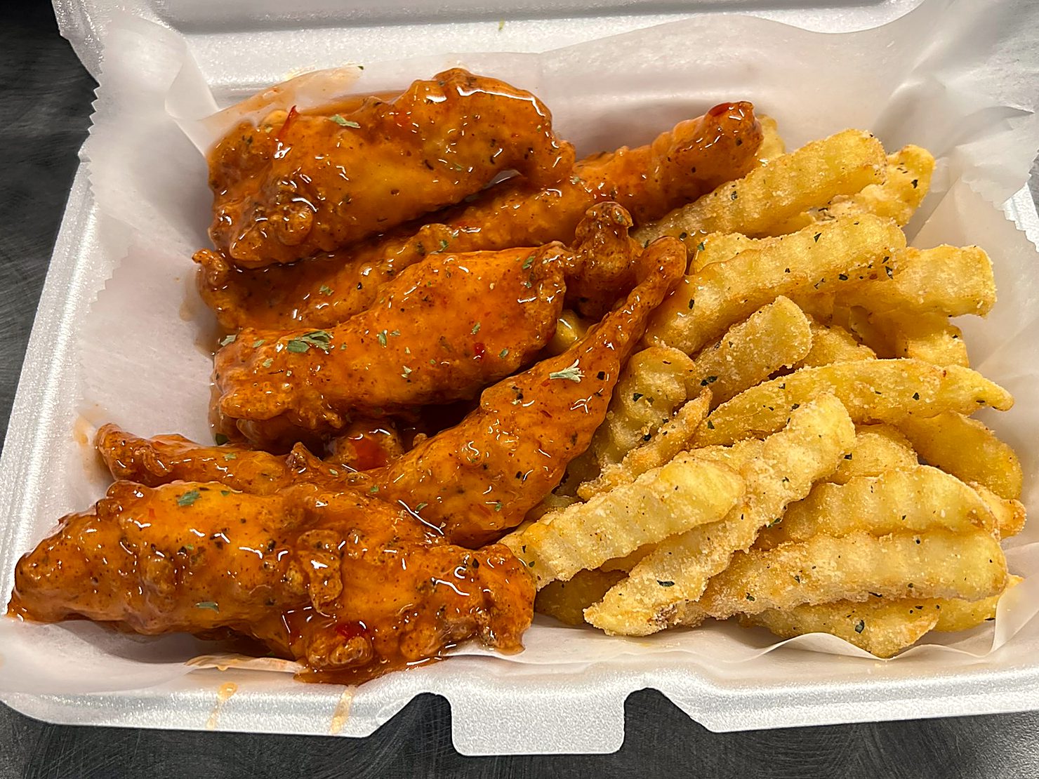 Sauced chicken tenders beside seasoned crinkle fries
